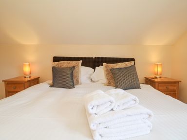 A bedroom with a double bed with pillows and folded towels and two wooden bedside tables with lamps at The Willows in Winnard's Perch near St Columb Major