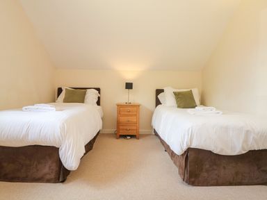 A bedroom with two single beds and a wooden nightstand with a lamp in between at The Willows Winnard's Perch near St Columb Major