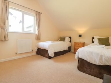 A bedroom with two single beds a bedside table with a lamp and a window with curtains at The Willows in Winnard's Perch near St Columb Major