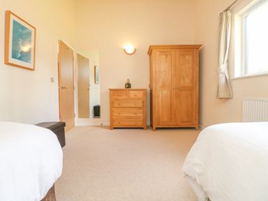 A bedroom with a wardrobe chest of drawers a mirror a window with curtains and two beds at The Willows Winnard's Perch near St Columb Major