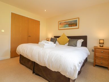 A bedroom with a bed with white linens pillows and folded towels beside a wooden nightstand with a lamp at The Willows Winnard's Perch near St Columb Major