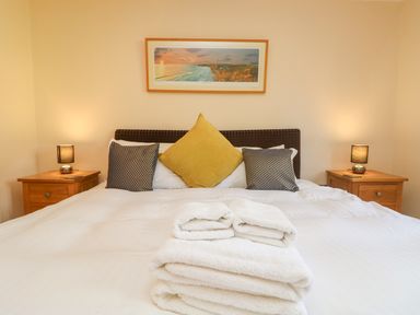 A bedroom with a large bed with pillows and folded towels on it two wooden bedside tables with lamps and a framed picture on the wall at The Willows in Winnard's Perch near St Columb Major