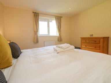 A bedroom with a bed with pillows and folded towels a wooden chest of drawers and a window with curtains at The Willows in Winnard's Perch near St Columb Major