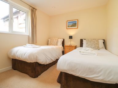 A bedroom with two single beds a wooden nightstand and a window at The Willows in Winnard's Perch near St Columb Major