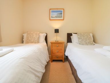 A bedroom with two single beds separated by a wooden nightstand with a lamp and a framed picture on the wall at The Willows Winnard's Perch near St Columb Major