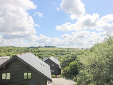 Houses with sloped roofs surrounded by greenery and fields under a partly cloudy sky at The Willows in Winnard's Perch near St Columb Major
