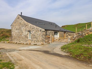 A stone house with a slate roof and wooden gate on a gravel driveway in a rural area at Beudy Mawr in Cwmystradllyn near Tremadog