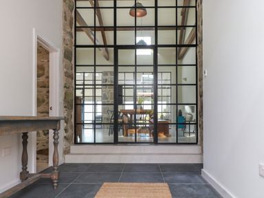 A hallway with a wooden table and tiled floor facing a glass partition with metal frames at Beudy Mawr in Cwmystradllyn near Tremadog
