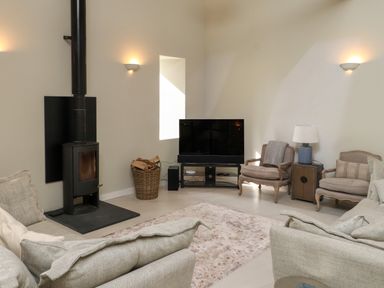 A living room with a wood stove a basket of firewood a television two armchairs a side table with a lamp and a sofa at Beudy Mawr in Cwmystradllyn near Tremadog