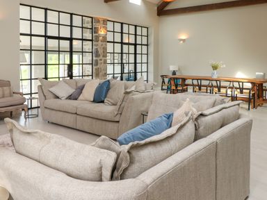 A living room with beige sofas and blue cushions near a wooden dining table with chairs and a vase with flowers at Beudy Mawr in Cwmystradllyn near Tremadog