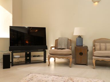 A living room with a television on a black glass stand two armchairs and a side table with a lamp at Beudy Mawr in Cwmystradllyn near Tremadog