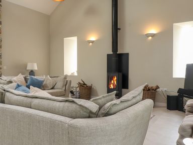 A living room with sofas a wood burning stove and baskets of firewood at Beudy Mawr in Cwmystradllyn near Tremadog