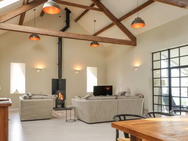 A living room with two beige sofas a wood stove and exposed wooden beams at Beudy Mawr in Cwmystradllyn near Tremadog