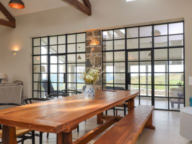 A dining area with a wooden table and bench with a vase of flowers on top and glass partition walls at Beudy Mawr in Cwmystradllyn near Tremadog
