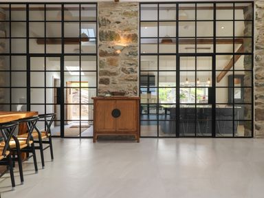 A dining area with wooden chairs and table separated by glass partition and stone walls at Beudy Mawr in Cwmystradllyn near Tremadog