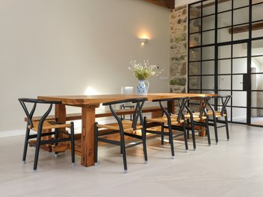 A dining area with a wooden table and black metal chairs near a stone wall and glass door at Beudy Mawr in Cwmystradllyn near Tremadog