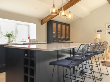 A kitchen with black cabinets an island with bar stools and pendant lights at Beudy Mawr in Cwmystradllyn near Tremadog