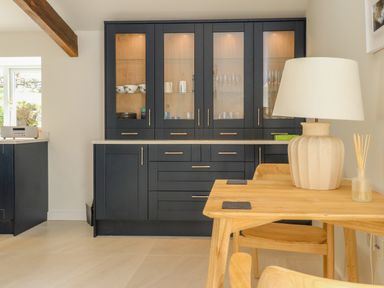 A kitchen area with black cabinets glass doors and a wooden table with a lamp at Beudy Mawr in Cwmystradllyn near Tremadog