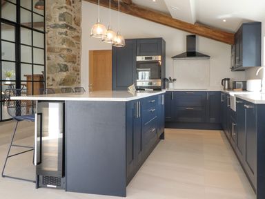 A kitchen with blue cabinets a wooden beam stone wall and three pendant lights at Beudy Mawr in Cwmystradllyn near Tremadog