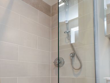 A tiled shower area with a glass panel and a handheld showerhead at Beudy Mawr in Cwmystradllyn near Tremadog