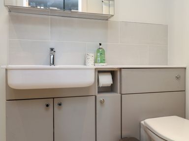 A bathroom sink with a soap dispenser and toilet paper holder with cabinets below at Beudy Mawr in Cwmystradllyn near Tremadog