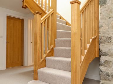 A carpeted staircase with wooden banisters next to a stone wall and wooden door at Beudy Mawr in Cwmystradllyn near Tremadog