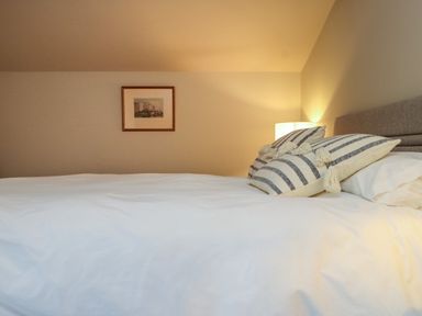 A bedroom with a bed with white linens striped pillows a bedside lamp and a framed picture on the wall at Beudy Mawr in Cwmystradllyn near Tremadog
