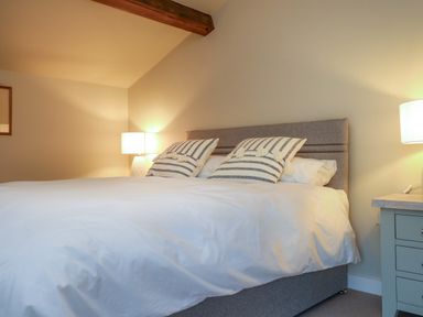 A bedroom with a double bed two striped pillows two bedside lamps and a wooden beam at Beudy Mawr in Cwmystradllyn near Tremadog