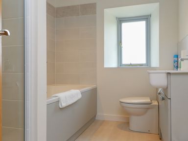 A bathroom with a bathtub towel on the edge a toilet under a window and a sink with cabinet at Beudy Mawr in Cwmystradllyn near Tremadog