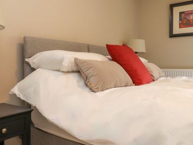 A bed with white bedding and beige and red pillows next to a bedside table and a lamp at Beudy Mawr in Cwmystradllyn near Tremadog