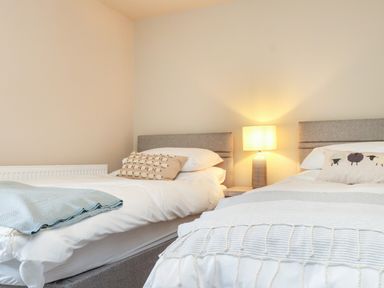 A bedroom with two single beds a bedside table with a lamp and sheep patterned cushions at Beudy Mawr in Cwmystradllyn near Tremadog