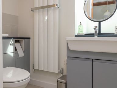 A bathroom with a toilet a round mirror a sink with soap a radiator and a small trash bin at Beudy Mawr in Cwmystradllyn near Tremadog