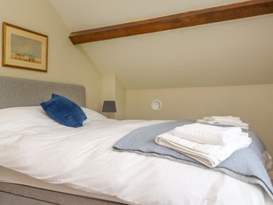 A bedroom with a bed with white linens a blue pillow folded towels on a blue blanket a lamp and a framed picture on the wall at Beudy Mawr in Cwmystradllyn near Tremadog