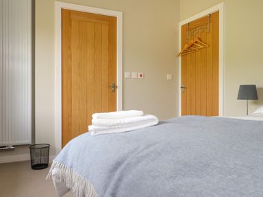 A bedroom with two wooden doors a bed with towels on it a bedside lamp and a trash bin at Beudy Mawr in Cwmystradllyn near Tremadog
