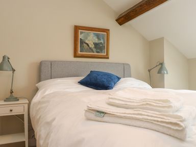 A bedroom with a bed holding white towels and a blue pillow and two bedside tables with lamps at Beudy Mawr in Cwmystradllyn near Tremadog