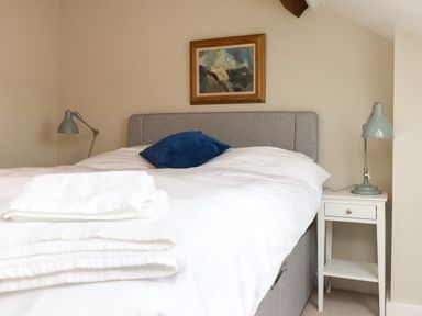 A bedroom with a gray bed, white bedding, a blue pillow, white towels on the bed, two bedside tables with lamps, and a framed painting on the wall at Beudy Mawr in Cwmystradllyn near Tremadog