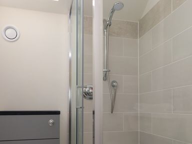 A shower area with a glass door and a handheld showerhead attached to tiled walls at Beudy Mawr in Cwmystradllyn near Tremadog