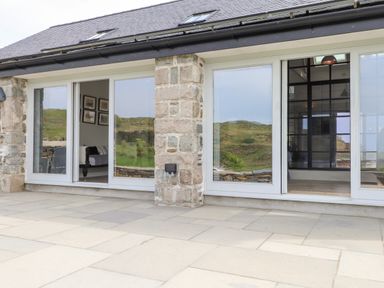 Stone house exterior with large glass sliding doors opening to a tiled patio at Beudy Mawr in Cwmystradllyn near Tremadog