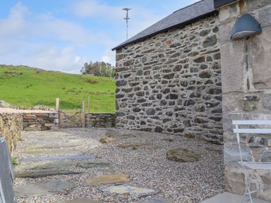 A stone wall building with a gravel path and wooden gate in a grassy rural area at Beudy Mawr in Cwmystradllyn near Tremadog