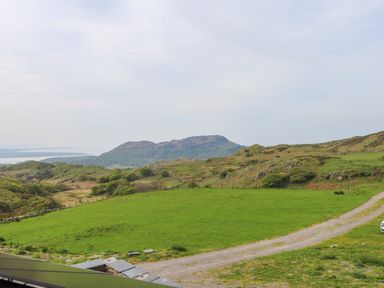 A grassy field with a dirt path leading toward hills and mountains in the distance at Beudy Mawr in Cwmystradllyn near Tremadog