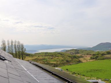Solar panels installed on a rooftop with green hills and a body of water in the background at Beudy Mawr in Cwmystradllyn near Tremadog