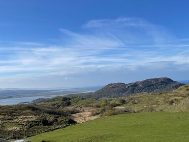 A landscape with green hills a body of water and a mountain at Beudy Mawr in Cwmystradllyn near Tremadog