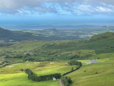A rural landscape with green hills a small house a road and the sea in the distance at Beudy Mawr in Cwmystradllyn near Tremadog