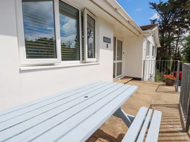 An outdoor patio area with a pale blue wooden bench and table near a white wall house entrance at Surf Break in Polzeath