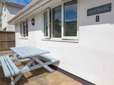 A blue picnic table and benches outside a white building with windows and a sign reading Surf Break 8 in Polzeath