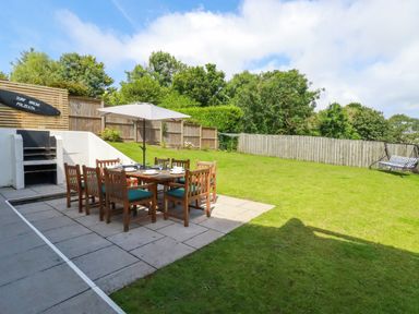 A backyard with a dining table and chairs under an umbrella a barbecue grill and a garden swing at Surf Break in Polzeath