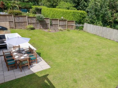 A garden with a patio dining table and chairs with plates and an umbrella at Surf Break in Polzeath