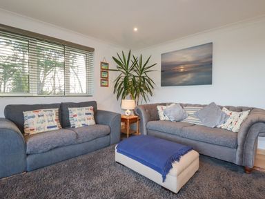 A living room with two sofas a blue throw on an ottoman a plant and a landscape painting at Surf Break in Polzeath