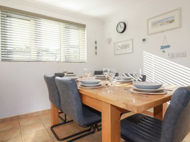 A dining room with a wooden table set for six and leather chairs with shoes at Surf Break in Polzeath