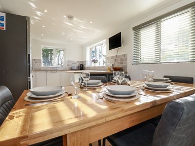 A kitchen with a wooden dining table set with plates and glasses and a window with blinds at Surf Break in Polzeath